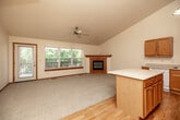 This two-story home offers five bedrooms and two full bathrooms across a well-organized layout, with the majority of the living space found on the upper floor. The main level features an open-concept kitchen and living room area with soaring vaulted ceilings that amplify the sense of space. The kitchen is equipped with warm honey-toned cabinetry, a center island with a white countertop, hardwood flooring, and a pendant chandelier, creating a bright and functional cooking space. The adjacent living room features plush carpeting, a ceiling fan, and large windows that invite abundant natural light and outdoor views, along with a door providing direct exterior access. A carpeted staircase with natural wood handrails and a chandelier overhead connects the two floors. The bedrooms are generously sized and carpeted, including a spacious primary bedroom. Both full bathrooms are finished with warm wood vanities, white countertops, tile flooring, and tub-shower combinations. The lower floor houses an attached garage with a standard roll-up door and a concrete floor, offering practical storage and parking. Neutral tones, wood trim detailing, and ceiling fans are consistent features throughout, giving the home a cohesive and comfortable character.