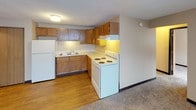 This 2-bedroom, 1-bathroom unit is laid out entirely on a single floor, offering a straightforward and efficient floor plan. The kitchen features warm-toned oak cabinetry arranged in an L-shaped configuration, providing ample storage and counter space. White appliances — including a refrigerator, electric coil range, and under-cabinet range hood — complement the light countertops, while durable wood-look flooring adds a clean, practical finish to the space.

The living area transitions from the kitchen and is finished with wall-to-wall carpet, offering a comfortable, casual atmosphere. A window unit provides supplemental cooling, and a baseboard heater ensures warmth throughout the colder months. The entry area includes a closet, adding convenient storage right at the door.

Both bedrooms are carpeted and feature neutral wall tones, baseboard heating, and windows that allow natural light to filter in. One bedroom includes two windows and the other is equipped with a built-in closet with a hanging rod, maximizing functionality.

The bathroom is finished with tile flooring and includes a wall-mounted sink, toilet, and mirrored medicine cabinet, offering a clean and utilitarian design. Textured ceilings are present throughout the unit, contributing to a consistent aesthetic across all rooms.
