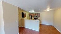 This single-floor unit offers a functional, open-concept layout with warm neutral tones throughout. The living area features hardwood-style flooring and a tiled fireplace with a classic mantel, creating a welcoming focal point. Natural light filters in through windows and a sliding glass door that opens to an outdoor space, enhancing the overall brightness of the unit.

The kitchen is designed for practicality and efficiency, featuring rich medium-toned cabinetry, granite-style countertops, and a peninsula that doubles as a breakfast bar, seamlessly connecting the kitchen to the living area. Stainless steel appliances — including a refrigerator, gas range, and over-the-range microwave — complete the kitchen's modern, cohesive look.

The bedroom is carpeted and offers a quiet, comfortable retreat, with a window providing natural light and views of greenery outside. The bathroom includes a full soaking tub with a shower, finished in clean white surrounds with chrome fixtures.

Hardwood-style flooring extends through the main living and kitchen areas, tying the open-plan space together cohesively. The unit's straightforward, well-organized design makes it a comfortable and practical living space.