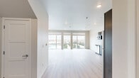 This well-designed two-bedroom, two-bathroom residence spans two floors, offering a thoughtful layout that balances open communal spaces with private retreats. The main level features a bright, open-concept living and kitchen area bathed in natural light from large floor-to-ceiling windows that frame expansive outdoor views of the surrounding cityscape and greenery. Light-toned hardwood flooring flows throughout, enhancing the clean, modern aesthetic. The kitchen is equipped with stainless steel appliances, including a range with a stainless steel hood vent, gray shaker-style cabinetry with open shelving, light stone countertops, and a white subway tile backsplash — a functional and stylish space for cooking. The two bathrooms mirror the home's contemporary finishes, featuring gray vanity cabinetry, stone countertops, and clean white walk-in showers. A staircase connects the two floors, leading to the upper level where the bedrooms are located. The spacious primary bedroom benefits from natural light and generous proportions. A dedicated walk-in closet with wire shelving provides ample storage. The secondary bedroom features a ceiling fan, a large window, and light hardwood flooring. Throughout, the home maintains a bright, neutral palette that creates a clean, airy atmosphere.