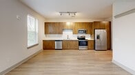 Located at 901 River Rd, Unit 201 in Charlottesville, Virginia, this thoughtfully designed unit offers a clean, modern aesthetic within a well-utilized single-floor layout. Light wood-tone flooring runs continuously throughout the space, creating a warm and cohesive feel that ties each area together seamlessly.

The open living area is bright and airy, benefiting from multiple windows dressed with horizontal blinds that invite natural light while maintaining privacy. A ceiling fan adds both comfort and a subtle design element to the room, while neutral wall tones keep the space feeling fresh and versatile.

The kitchen is a standout feature, boasting rich wood-grain cabinetry that extends from floor to ceiling, offering generous storage. White quartz-style countertops and a classic white subway tile backsplash provide a crisp contrast to the warm cabinetry. A full suite of stainless steel appliances — including a refrigerator, electric range, over-the-range microwave, and dishwasher — makes this kitchen as functional as it is attractive. Track lighting overhead ensures the space is well-lit.

The bathroom is clean and functional, featuring a full soaking tub and shower combination finished in white tile, complemented by brushed nickel hardware for a polished look. The overall ambiance of the unit is modern, bright, and move-in ready.