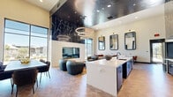 Located at 3811 Commerce Way in Sacramento, CA, this single-floor living space delivers a striking contemporary design that balances bold aesthetics with functional versatility. The focal point of the room is a dramatic floor-to-ceiling black marble accent wall with vivid white veining, framing a sleek see-through fireplace and anchoring the space with undeniable visual impact. Suspended above is a tiered arrangement of circular pendant lights that cast warm, ambient illumination throughout.

The herringbone-patterned wood flooring grounds the space with warmth and texture, flowing seamlessly across multiple seating and activity zones. A comfortable lounge area features plush leather armchairs arranged around a sculptural marble-topped coffee table, ideal for relaxed gatherings. Nearby, a long white counter with bar-height seating provides a casual dining or work surface, complemented by a row of stylish upholstered chairs.

A dedicated dining area along one wall offers white-topped tables paired with rust-colored chairs, accented by ornate framed mirrors and curated botanical wall art. Floor-to-ceiling glass windows and a set of elegant dark double doors flood the interior with natural light while offering views of the surrounding outdoor landscape. The high ceilings amplify the sense of openness, making this a sophisticated and inviting communal space.