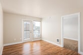 This single-floor residential unit offers a thoughtfully designed layout with a clean, neutral aesthetic throughout. The living areas feature warm hardwood-style flooring that extends through the main spaces, complemented by crisp white baseboards and soft, neutral-toned walls that create a bright and welcoming atmosphere. A glass-paneled door in the living area leads to the outdoors, allowing abundant natural light to flow in alongside views of the surrounding urban environment.

The kitchen is a standout feature, outfitted with rich dark cabinetry, white countertops, a subway tile backsplash, and a full suite of stainless steel appliances including a refrigerator, electric range, dishwasher, and microwave. Track lighting overhead adds both function and style to this efficient galley-style space.

The bedrooms are finished with plush carpeting for added comfort, each featuring windows that bring in natural light and views of the neighborhood. One bedroom includes direct access to a private en-suite bathroom with dark cabinetry and tile flooring, as well as a dedicated walk-in closet. Additional bedrooms offer generous proportions and baseboard heating. A central hallway connects the rooms with ease, providing a practical and cohesive flow throughout the unit.