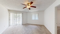 This single-floor residence offers a thoughtfully designed layout with a comfortable, functional flow throughout. The living area is generously sized, featuring neutral-toned wall-to-wall carpeting, a textured ceiling, and a ceiling fan with integrated lighting. Large sliding glass doors flood the space with natural light while providing outdoor views, complemented by an additional window fitted with vertical blinds.

The kitchen is outfitted with white cabinetry, dark granite-style countertops, a white subway tile backsplash, and wood-look vinyl plank flooring. Black appliances, including a refrigerator, range, and over-the-range microwave, lend a cohesive, contemporary look to the space.

The bedrooms continue the carpeted aesthetic and are each equipped with ceiling fans, vertical blinds, and louvered bi-fold closet doors, offering ample storage. Natural light enters through windows in each room, creating a bright and airy atmosphere.

The bathrooms are finished with white cabinetry, dark granite-style countertops, large wall-mounted mirrors, and well-lit vanities. One bathroom includes a full soaking tub with tiled surround. Both bathrooms maintain a clean, understated design consistent with the rest of the home. Overall, the space presents a neutral, move-in ready environment suitable for a variety of living arrangements.