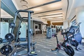 Located at 882 Juniper St NE in Midtown Atlanta, this fitness center presents a polished, contemporary design across a single open floor. The space is defined by expansive floor-to-ceiling windows along its perimeter, flooding the interior with natural light while offering views of the surrounding Atlanta skyline and landscaped greenery below.

The layout is thoughtfully organized, with distinct zones dedicated to cardio and strength training. The cardio section features stair climbers, treadmills, and stationary bikes positioned near the large windows to maximize the outdoor views during workouts. The strength training area is well-equipped with cable machines, a power rack with free weights, and a range of selectorized machines arranged for efficient use of the space.

Architectural details include a curved ceiling with recessed and linear lighting, dark wood accent columns, and patterned carpet flooring that adds a refined, boutique feel. Full-length mirrors are strategically placed throughout the strength area to support form and enhance the sense of depth. The overall ambiance is upscale and functional, combining modern design with a comprehensive array of fitness equipment suited for a full-body workout.