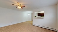 This single-floor residence offers a practical and well-organized layout across several connected living areas. The combined living and dining space is generously sized, finished with neutral wall-to-wall carpeting and bright white walls that create a clean, open atmosphere. A ceiling fan with integrated lighting anchors the living area, while a chandelier adds a decorative touch to the dining zone. A pass-through window connects the dining area directly to the kitchen, enhancing the sense of openness between the spaces.

The kitchen features dark espresso cabinetry paired with stainless steel appliances, including a gas range, microwave, and refrigerator. White subway tile backsplash and wood-look vinyl flooring complete the functional, modern aesthetic. A window above the counter allows natural light to brighten the workspace.

Both bedrooms are carpeted and equipped with ceiling fans. The primary bedroom includes a double sliding-door closet and ample floor space, while the second bedroom features a window with natural light and baseboard heating. Each room offers a calm, neutral palette suitable for a variety of uses.

The bathroom is neatly finished with gray walls, a white toilet, and a tub-shower combination enclosed by a striped curtain. Baseboard heating is present throughout the unit, supplemented by a wall-mounted HVAC unit in one bedroom.