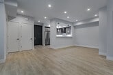 Located at 5955 Saturn St in Los Angeles, this single-floor residence showcases a clean, contemporary design throughout. The open-concept living area is anchored by light hardwood flooring, recessed lighting, and a sleek built-in fireplace flanked by a built-in shelving unit. Large black-framed windows flood the space with natural light and offer views of the surrounding neighborhood's mature trees. A dedicated sitting area features an oversized picture window and direct access via a black-framed glass door. The kitchen is thoughtfully designed with warm wood-tone cabinetry, stainless steel appliances including a French door refrigerator and gas range with a professional hood, white quartz countertops, and a pass-through counter with pendant lighting that connects to the dining area. The bedrooms feature plush carpeting, tray ceilings, recessed and pendant lighting, generous closet space with built-in shelving, and large windows. The bathrooms include tiled tub-shower combinations with glass enclosures and warm hexagonal tile flooring. Throughout the unit, a neutral color palette of crisp whites and soft grays reinforces a bright, modern ambiance.