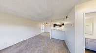 Located at 4255 S Tamarus St in Las Vegas, NV, this two-story, one-bedroom, two-bathroom unit offers a practical and well-organized layout across two floors. The main level features an open living room with plush carpet flooring, a ceiling fan, and a sliding glass door fitted with vertical blinds that allows natural light to fill the space. Adjacent to the living area is a pass-through kitchen, equipped with dark cabinetry, white appliances including a coil-top range and refrigerator, light wood-look flooring, a skylight, and ample overhead storage. A half bathroom on the main floor features a light-toned quartz-style countertop, a large wall mirror, and chrome fixtures. A staircase leads to the upper level, where the spacious primary bedroom is carpeted and includes a closet with bi-fold doors and a dedicated HVAC vent. The upper-level full bathroom features wood-look flooring, a tub-shower combination, a single vanity with undermount sink, and built-in cabinetry. Two closets throughout the unit provide generous storage. Textured ceilings are consistent throughout both floors, contributing to the cohesive and neutral aesthetic of the home.