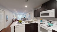 This single-floor unit in Spartanburg, SC, offers a thoughtfully designed open-concept layout that seamlessly connects the kitchen, dining, and living areas. Rich hardwood-style flooring flows throughout, providing a warm and cohesive aesthetic.

The kitchen is a functional centerpiece, featuring dark espresso cabinetry paired with crisp white countertops and white appliances, including a range, built-in microwave, dishwasher, and full-size refrigerator. A peninsula with a double sink creates a natural divide between the kitchen and the adjacent dining area, making the space ideal for both cooking and entertaining. Recessed lighting illuminates the open living and dining zone, which extends toward a sliding glass door offering outdoor access and natural light.

The living room is generously proportioned, with recessed lighting and a neutral gray color palette that creates a calm, inviting atmosphere. The bedrooms feature ceiling fans, windows with natural light, and hardwood-style flooring, with one bedroom offering direct access to a private bathroom. The bathrooms are finished with dark vanity cabinetry, white countertops, and large mirrors, maintaining a consistent design language throughout the unit.