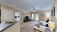 Located on Rosebud Court Ave in Loganville, Georgia, this single-floor residence offers a well-designed, open layout with warm neutral tones and crown molding throughout. The living room is bright and spacious, featuring plush carpeting, a ceiling fan, floating wall shelves, and a glass door that opens to the outdoors, allowing natural light to fill the space. The kitchen is equipped with rich dark-wood cabinetry, granite-style countertops, and black appliances including a refrigerator, electric range, and built-in microwave, all complemented by wood-look flooring. Adjacent to the kitchen, a peninsula counter connects seamlessly to the open dining and living areas. The dedicated dining space accommodates a full table and chairs, finished with crown molding and carpeted floors. A thoughtfully integrated built-in desk nook provides a convenient workspace. The bedroom is generously sized with carpet, a ceiling fan, and a large window with views of surrounding greenery. The bathroom features dark wood cabinetry, a wide vanity mirror, and wood-look flooring. A dedicated laundry area houses a full-size washer and dryer with overhead shelving, adding everyday practicality to this well-appointed residence.