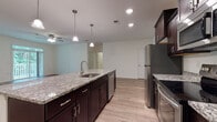 This single-story residence offers a thoughtfully designed layout with modern finishes throughout. The kitchen serves as a central hub, showcasing rich dark cabinetry paired with granite countertops and a generously sized island that doubles as a breakfast bar. Pendant lighting illuminates the island, while recessed lighting brightens the space overall. Stainless steel appliances, including a refrigerator, range, microwave, and dishwasher, complete the kitchen's functional and contemporary aesthetic. Light wood-look flooring extends through the kitchen and adjoining living area, creating a cohesive, open feel.

The bedrooms feature plush carpeting and ceiling fans, offering a comfortable retreat. Natural light filters through blinded windows, with views of greenery outside. Each bedroom includes closet storage, with at least one room featuring a set of double doors for added convenience.

Two bathrooms serve the residence: one equipped with a tub-shower combination and the other with a walk-in shower. Both feature consistent granite-topped dark vanities and wood-look flooring, maintaining the home's unified design language. The overall aesthetic is clean, modern, and move-in ready.