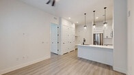 Located at 2825 W 11th St in Houston's desirable Garden Oaks neighborhood, this one-bedroom, one-bathroom unit offers a thoughtfully designed single-floor layout with a clean, contemporary aesthetic. Light-toned wood-look flooring runs throughout the space, complementing a bright, neutral color palette that enhances the sense of openness.

The open-concept kitchen and living area serves as the centerpiece of the unit. The kitchen is well-appointed with crisp white shaker-style cabinetry, white quartz countertops, stainless steel appliances including a French door refrigerator, gas range, and built-in microwave, and a large island with an undermount sink and matte black faucet. Cylindrical glass pendant lights hang above the island, adding a modern touch. A built-in wine rack provides additional storage and character.

The bedroom is a comfortable, well-proportioned space featuring a ceiling fan and a trio of large windows fitted with horizontal blinds that frame direct views of the outdoor pool area, allowing ample natural light. The bathroom includes a glass-enclosed walk-in shower with marble-style tile, matte black hardware, and direct access to a dedicated walk-in closet with built-in shelving, combining style with practical storage.
