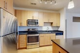 Located at 2677 Avenir Pl in Vienna, VA, this well-appointed single-floor residence offers one bedroom, two full bathrooms, and a versatile den within a thoughtfully designed layout. The open-concept living and dining area is bathed in natural light, showcasing gleaming hardwood floors and a pass-through architectural detail that connects the space to the kitchen area. The kitchen is a standout feature, equipped with stainless steel appliances including a refrigerator, electric range, and built-in microwave, complemented by light maple cabinetry, dark stone countertops, and a generous island with pendant lighting overhead. A dedicated entrance leads into the home, which also includes a convenient in-unit laundry area and four closets providing ample storage. The carpeted primary bedroom connects to a full bathroom and offers a calm, comfortable retreat. The second bathroom mirrors the same clean aesthetic, featuring white subway tile surrounds, soaking tubs, tile flooring, and brushed nickel fixtures. The flexible den is carpeted and well-suited for a home office or guest space. A private balcony extends the living area outdoors, completing this functional and stylish Vienna residence.