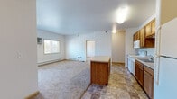Located at 1900 Dakota Dr N in Fargo, North Dakota, this single-floor residence offers three bedrooms, three bathrooms, and three closets within a practical and well-organized layout. The kitchen is a standout feature, equipped with warm-toned wood cabinetry, a central island with a laminate countertop, white appliances including a range, dishwasher, and refrigerator, and durable tile flooring in an earthy stone pattern. The open sightline from the kitchen into the living area creates a connected, functional flow. The bedrooms are carpeted and finished with neutral walls, offering a clean and versatile canvas. Each room benefits from natural light through wood-trimmed windows with blinds, and select rooms include wall-mounted air conditioning units alongside baseboard heating for year-round climate control. The primary bedroom provides a comfortable footprint with access to a dedicated closet. The bathrooms are finished with the same tile flooring found in the kitchen, and feature warm wood vanities with light countertops. One bathroom includes a full tub-shower combination, while another offers a double-sink vanity with a large mirror. The overall aesthetic is straightforward and functional, with consistent finishes throughout that create a cohesive and easy-to-maintain living environment.