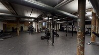 This single-floor fitness facility in South Carolina blends industrial character with comprehensive workout functionality. The space retains its historic bones throughout, showcasing exposed brick walls with aged, layered paint, original structural columns, and overhead ductwork running across the ceiling — all grounded by durable rubber flooring suited for high-intensity use.

The main training floor is generously sized, accommodating multiple functional fitness rigs equipped with barbells, weight plates, and battle ropes, alongside a dedicated heavy bag station featuring a UFC punching bag and speed bag. A separate strength training area houses a range of selectorized cable and resistance machines positioned along mirrored and open walls, providing ample space for individual circuit training.

A distinct open room features exposed brick walls and natural light from street-level windows, furnished with medicine ball racks and open floor space ideal for functional or group training. The facility also includes a dedicated cardio zone with treadmills and a spin studio outfitted with cycling bikes and a wall-mounted television. Fluorescent and track lighting illuminate each area effectively throughout.