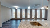 Located at 3010 Trier Rd in Fort Wayne, Indiana, this well-appointed single-floor unit offers a clean, contemporary design throughout. The open-concept living and kitchen area is a standout feature, anchored by a granite-topped island with an undermount sink and pendant lighting overhead. A row of tall, evenly spaced windows lines the living area wall, flooding the space with natural light and offering pleasant outdoor views. Rich, dark hardwood-style flooring runs throughout the main living areas, complementing the neutral taupe wall tones.

The kitchen is outfitted with white cabinetry, granite countertops, and stainless steel appliances including a range, over-the-range microwave, and refrigerator. Dual closet doors off the main living area provide generous storage options. The bedrooms feature plush carpeting and are generously lit by large windows, with one bedroom benefiting from a wraparound window arrangement that offers a bright, airy atmosphere.

The bathroom continues the consistent design language with granite countertops, white cabinetry with brushed nickel hardware, a large vanity mirror, and hardwood-style flooring. Grab bars and a clean, accessible layout add a thoughtful, functional touch. Throughout the unit, textured ceilings and flush and pendant lighting fixtures complete the polished, modern aesthetic.