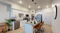 This well-designed single-floor residence offers a thoughtful layout that balances comfort and functionality throughout. The heart of the home is a contemporary open-concept kitchen featuring crisp white cabinetry with matte black hardware, a white subway tile backsplash, quartz-style countertops, and a full suite of stainless steel appliances including a refrigerator, electric range, microwave, and dishwasher. A central island with pendant lighting above provides additional prep space and casual bar seating, flowing seamlessly into the connected living area. The living room is bright and airy, benefiting from large windows and a sliding glass door that opens to a private outdoor area, complemented by a ceiling fan and light wood-style flooring that extends throughout the main living spaces. Two comfortable bedrooms are finished with plush carpeting and windows that invite natural light, offering a calm and restful retreat. The full bathroom includes a wide vanity with white cabinetry, a quartz-style countertop, an undermount sink, and a shower-tub combination. A dedicated in-unit laundry area with side-by-side washer and dryer and built-in shelving adds everyday convenience. A walk-in pantry or storage closet off the kitchen rounds out the practical amenities of this well-appointed space.