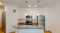 This single-story residence in Leander, Texas offers a clean, modern design with a cohesive neutral palette throughout. Light wood-tone flooring extends across the main living areas, lending warmth and continuity to the open layout. The living area is generously proportioned, with white walls and recessed lighting that enhance the bright, airy atmosphere. A glazed entry door allows additional natural light to fill the space.

The kitchen serves as a functional centerpiece, featuring a granite-topped peninsula with an undermount sink and pendant lighting overhead. White upper cabinetry reaches toward the ceiling, complemented by warm wood-toned lower cabinets and a classic white subway tile backsplash. Stainless steel appliances, including a range, built-in microwave, and refrigerator, complete the well-equipped cooking space.

The bedroom offers plush carpeting underfoot, a ceiling fan with light fixture, and a double window fitted with blinds for natural light and privacy. A closet is accessible directly from the room. The hallway connecting the spaces is fitted with recessed lighting, a wall-mounted security panel, and smooth white walls.

The bathroom is finished with tile flooring, a tub-shower combination with tile surround, a granite-topped vanity with a wood base cabinet, and chrome fixtures, reflecting the consistent, contemporary finishes found throughout the home.