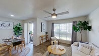 This well-appointed single-floor residence offers a thoughtfully designed layout that balances comfort and functionality. The living room serves as the heart of the home, featuring warm hardwood-style flooring, a ceiling fan with light, and generous natural light streaming through large windows dressed with gray curtain panels and horizontal blinds. A sliding glass door connects the living area to an outdoor patio, enhancing the sense of openness. The space is styled with a neutral, modern-casual aesthetic that carries throughout the home.

The kitchen is efficiently laid out with rich dark cabinetry, black appliances including a refrigerator, electric range, and over-the-range microwave, complemented by light countertops and a classic tile backsplash. Adjacent to the kitchen, the dining area accommodates a full-sized table and benefits from recessed lighting and continued hardwood-style flooring.

Both bedrooms are comfortably sized, each featuring a ceiling fan, ample natural light from multiple windows, and walk-in or reach-in closets. One bedroom includes direct outdoor access, adding a distinctive touch.

The bathroom is clean and functional, offering a combined tub and shower, a vanity with light stone-style countertops, and wood-look flooring that ties the space together cohesively.