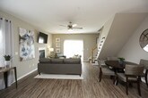 This two-story home offers a thoughtfully designed layout across both levels, connected by a prominent staircase with classic wood railings visible from the open upper floor. The living room serves as a central gathering space, featuring hardwood-style flooring, a ceiling fan, a sleek fireplace framed in white trim, and a sliding glass door that opens to an outdoor patio, filling the room with natural light. The kitchen is well-equipped with warm oak cabinetry, light countertops, a double stainless steel sink, and stainless steel appliances including a dishwasher, electric range, and over-the-range microwave. Multiple bedrooms are spread across both floors, each finished with plush carpeting and ceiling fans. The primary bedroom includes a window with natural light and direct access to an en-suite. A secondary bedroom features neutral tones and a charming vanity area. The bathrooms include a full bath with hardwood-style flooring, a tub-shower combination, and warm wood vanity cabinetry, as well as a compact half bath with a decorative shelf. Throughout the home, neutral gray and beige tones create a calm, cohesive atmosphere well-suited for comfortable everyday living.