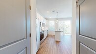Located at 3250 Buford Hwy in Duluth, GA, this single-floor unit offers a clean, modern aesthetic throughout. The open-concept layout centers around a well-appointed kitchen featuring crisp white shaker cabinetry, granite countertops, a white subway tile backsplash, and a full suite of stainless steel appliances including a refrigerator, range, microwave, and dishwasher. A central island with matching granite provides additional prep space and casual seating, illuminated by elegant pendant lighting overhead. Recessed lighting and large windows allow natural light to fill the space generously.

The warm-toned wood-style flooring extends seamlessly throughout the living areas, adding a sense of continuity and warmth to the bright, neutral color palette. The living area benefits from multiple windows dressed with horizontal blinds, along with direct access to a private balcony that offers pleasant outdoor views of the surrounding greenery and neighborhood.

The additional rooms maintain the same clean, light-filled character, with white walls and consistent flooring providing a versatile canvas. The overall ambiance of the space is contemporary and inviting, combining functional design with quality finishes that are well-suited for comfortable everyday living.