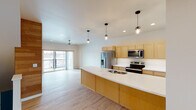 This three-floor unit in Sheboygan, Wisconsin offers a well-designed layout with contemporary finishes and practical amenities. The ground level features a spacious attached garage with a large automatic door, overhead lighting, and an interior entry point that connects to the main living areas via a sliding glass door and foyer space.

The main living floor showcases an open-concept design anchored by a kitchen with warm honey-toned cabinetry, white quartz countertops with subtle veining, and a generous curved island with a stainless steel undermount sink. Pendant lighting in an industrial style illuminates the workspace, while stainless steel appliances—including a refrigerator, electric range, and over-the-range microwave—complete the setup. The kitchen flows seamlessly into the living area, which features light wood-look flooring and a sliding glass door opening to a private balcony with outdoor views.

The two bedrooms offer plush carpeting, recessed lighting, and ample closet space. One bedroom includes a sliding door to a second balcony. The two bathrooms feature light wood vanities, white countertops, and tile flooring. The full bath includes a tub-shower combo and a window for natural light, while the second bath provides a clean, functional design with a well-lit vanity mirror.