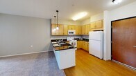Located at 5160 160th St SE in Prior Lake, Minnesota, this single-floor unit offers a thoughtfully designed layout that balances functionality and comfort. The open-concept kitchen and living area serves as the heart of the space, where rich dark granite countertops contrast beautifully with light maple cabinetry. A peninsula with pendant lighting above provides both additional prep space and a casual dining option. White appliances, including a refrigerator, electric range, microwave, and dishwasher, complete the kitchen. Hardwood-style flooring runs through the kitchen, transitioning to plush carpeting in the living area, which benefits from large windows that invite generous natural light and provide views to the exterior. Two full bathrooms are present in the unit. The primary bathroom features a vanity with warm maple cabinetry, a white countertop, a large mirror with overhead lighting, and stone-look tile flooring. The second bathroom mirrors this design aesthetic and includes a shower-tub combo with a colorful curtain and similarly styled vanity. Throughout the unit, neutral wall tones, clean lines, and consistent finishes create a cohesive and inviting atmosphere.