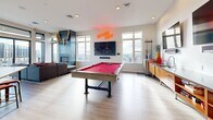 Located in Denver's 80211 zip code, the Sky Lounge is a thoughtfully designed rooftop amenity space that blends modern aesthetics with an energetic, social atmosphere. The single-floor layout offers a generous, open-concept living area bathed in natural light from large, floor-to-ceiling windows and expansive glass doors that frame panoramic views of the Denver skyline and surrounding neighborhoods.

The space is anchored by a bold red billiards table set atop light hardwood-style flooring, which serves as the centerpiece of the entertainment area. A glowing neon sign adds a vibrant, playful accent to the crisp white walls. Adjacent to the game area, a wet bar with warm wood cabinetry, a stainless steel refrigerator, a kegerator, and dual wall-mounted flat-screen televisions with soundbars create an ideal setup for gatherings.

A comfortable lounge zone features a plush sectional sofa, a sleek coffee table, and a fireplace framed by a dark accent wall — complemented by eclectic décor including mounted antlers. A dining and high-top bar seating area lines one wall, accented by framed abstract artwork and wall sconces, providing additional space for guests. The overall ambiance is modern, lively, and welcoming — an ideal rooftop retreat for socializing above the city.