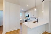 Located at 4418 Oat Grass Circle in Charlotte, NC, this modern three-story home offers a clean, contemporary design with consistent light-toned hardwood flooring and crisp white walls throughout. The ground floor provides a spacious garage with tile flooring and direct interior access through a hallway entrance. The main living level features an open-concept kitchen and living area filled with natural light. The kitchen is appointed with white shaker cabinetry, white quartz countertops, a subway tile backsplash, stainless steel appliances, and a large peninsula island with a matte black faucet and pendant lighting. A pantry and dedicated dining area complete this level, along with a convenient half bathroom. Elegant wood-tread staircases with black metal railings connect all three floors, adding a striking visual element. The upper floor hosts two well-proportioned bedrooms, each bathed in natural light from multiple windows offering outdoor views. The primary bedroom includes its own closet, while a total of four closets are distributed across the home for ample storage. Three full bathrooms feature white vanities with quartz countertops and matte black fixtures, maintaining a cohesive modern aesthetic. A laundry room adds everyday convenience to this thoughtfully designed home.