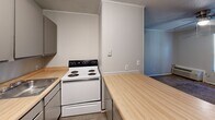 Located at 600 Folmar St in Troy, Alabama, this compact one-bedroom, one-bathroom unit offers a practical and efficient single-floor layout. The open living area flows directly into the kitchen, which is defined by a peninsula with warm butcher block countertops — offering both additional prep space and a natural visual divider. The kitchen is equipped with white appliances including a coil-burner electric range and a full-size refrigerator, complemented by gray upper cabinetry and a single-basin sink. A textured ceiling and crown molding add modest architectural character throughout. Soft carpet runs through the living room and bedroom, contributing to a warm, understated ambiance. The bedroom is a comfortable size, featuring a ceiling fan with light fixture, vertical panel-style wall accents, and a window that allows natural light to filter in. Convenient direct access to both a dedicated closet and the full bathroom is available from within the bedroom. The bathroom includes a full-size tub and shower combination with chrome fixtures. Ceiling fans are present in both the living area and bedroom, providing year-round comfort. The overall layout is straightforward and well-organized, making efficient use of the available space.