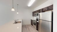 This well-appointed single-floor residence offers a clean, modern aesthetic with a thoughtful layout designed for comfortable living. The open-concept kitchen is a standout feature, outfitted with rich dark-espresso cabinetry, light quartz countertops, and a full suite of stainless steel appliances including a refrigerator, electric range, and over-the-range microwave. Elegant pendant lighting hangs above the sink, adding a refined touch, while light wood-look laminate flooring ties the kitchen and main living areas together seamlessly. The spacious living area is bathed in natural light from large sliding glass doors and windows fitted with horizontal blinds, creating a bright and airy atmosphere. Multiple interior doors along the hallway provide access to the bedrooms and closets, offering excellent storage and privacy. The bedrooms feature plush neutral carpeting and windows with natural views. A generously sized walk-in closet with wire shelving provides ample organization space. Two bathrooms serve the residence: one features a tub-shower combo with tile surround, a white vanity, and large-format tile flooring; the other includes a standalone walk-in shower, a wide vanity with under-cabinet storage, and matching tile flooring. The overall design is cohesive, neutral, and move-in ready.