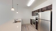This well-appointed single-floor residence offers a clean, modern aesthetic with a thoughtful layout designed for comfortable living. The open-concept kitchen is a standout feature, outfitted with rich dark-espresso cabinetry, light quartz countertops, and a full suite of stainless steel appliances including a refrigerator, electric range, and over-the-range microwave. Elegant pendant lighting hangs above the sink, adding a refined touch, while light wood-look laminate flooring ties the kitchen and main living areas together seamlessly. The spacious living area is bathed in natural light from large sliding glass doors and windows fitted with horizontal blinds, creating a bright and airy atmosphere. Multiple interior doors along the hallway provide access to the bedrooms and closets, offering excellent storage and privacy. The bedrooms feature plush neutral carpeting and windows with natural views. A generously sized walk-in closet with wire shelving provides ample organization space. Two bathrooms serve the residence: one features a tub-shower combo with tile surround, a white vanity, and large-format tile flooring; the other includes a standalone walk-in shower, a wide vanity with under-cabinet storage, and matching tile flooring. The overall design is cohesive, neutral, and move-in ready.