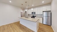 This well-appointed single-floor home offers three bedrooms, two full bathrooms, and a thoughtfully designed layout that maximizes comfort and functionality. The open-concept kitchen and living area serves as the heart of the home, anchored by a large center island with a quartz countertop, an undermount sink with a pull-down faucet, and elegant pendant lighting overhead. White shaker cabinetry, a subway tile backsplash, and stainless steel appliances — including a refrigerator, electric range, and microwave — complete the kitchen's clean, contemporary aesthetic. Light wood-look flooring flows throughout the main living areas, enhancing the bright, airy atmosphere. The living area features sliding glass doors that open to a balcony, allowing natural light to pour in. The three bedrooms are finished with plush wall-to-wall carpet and neutral tones, providing a calm retreat. The generously sized primary bedroom offers ample space and its own closet. Both bathrooms mirror the home's modern design, featuring white cabinetry with brushed nickel hardware, stone-toned countertops, undermount sinks, and full tub-shower combinations with light wood-look flooring. A dedicated laundry room with full-size washer and dryer hookups and wire shelving adds everyday convenience. Three closets provide abundant storage throughout.