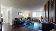 This single-floor residence offers a thoughtfully designed layout that balances comfort and functionality throughout. The living room serves as the centerpiece of the space, featuring rich dark hardwood flooring, a textured ceiling, and a large window that frames urban city views, filling the room with natural light. A bold blue patchwork area rug anchors the seating area, complemented by a dark credenza and wall art that adds character to the space.

The open flow leads into a dedicated dining area, where a round dark wood table sits beneath an elegant chandelier, positioned adjacent to a sliding glass door that further connects the interior to the surrounding cityscape. The galley-style kitchen is efficiently designed with dark cabinetry, light countertops, tiled flooring, stainless steel appliances including a range and over-the-range microwave, and a glass tile backsplash.

The bedroom offers a serene retreat with plush wall-to-wall carpeting, a large window with city views, and a built-in closet with sliding doors. The bathroom features classic white subway tile surrounding a full soaking tub and shower combination, tile flooring, and dark cabinetry at the vanity, providing a clean and functional finish.