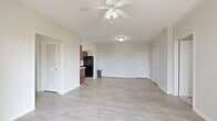 Located at 7855 Kitty Hawk Rd in Converse, TX, this single-story, 2-bedroom, 2-bathroom home offers a well-organized layout with a bright, open feel throughout. The spacious living area features light wood-look flooring and a ceiling fan with light fixture, creating a clean and airy atmosphere. It flows seamlessly toward the entry and into the hallway connecting the rest of the home.

The galley-style kitchen is outfitted with rich dark wood cabinetry, light countertops, a double sink, and black stainless appliances including a refrigerator, range, microwave, and dishwasher. A window above the counter brings in natural light.

Both bedrooms are carpeted and include ceiling fans, windows with blinds, and closet access. The generously sized primary bedroom features a walk-in closet with wire shelving extending along two walls, offering ample storage. The two bathrooms are finished with matching dark wood vanities, light countertops, and wood-look tile flooring.

Additional features include a dedicated laundry area, three closets total, and a private balcony with a wooden deck and metal railing that opens to a sweeping view of the surrounding landscape and open green space — a standout feature of this well-appointed home.