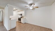 This single-floor residence offers a clean, functional layout with a bright and open feel throughout. The living area is spacious and airy, finished with light wood-look flooring and a ceiling fan with integrated lighting. Large sliding glass doors dressed with vertical blinds fill the room with natural light and provide access to the outdoors. The layout flows seamlessly into a well-designed kitchen, which features white cabinetry, marble-look countertops, and stainless steel appliances including a range, microwave, and dishwasher. Track lighting illuminates the workspace efficiently, and the same wood-look flooring carries through from the living area, creating a cohesive feel. The bedroom is generously sized, finished with plush carpeting and a window fitted with horizontal blinds. A full-width mirrored sliding closet provides ample storage while reflecting light throughout the room. The bathroom is neatly appointed with a white vanity, marble-look countertop, a large wall mirror, wood-look flooring, and a glass-panel shower enclosure. Textured ceilings are present throughout the unit, and the overall neutral color palette of whites and warm beiges lends the space a clean, move-in-ready aesthetic.
