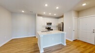 Located at 1001 Cox Grade Rd in Panama City Beach, Florida, this thoughtfully designed single-floor residence offers a clean, modern aesthetic throughout. The open-concept layout seamlessly connects the kitchen and living area, creating a bright and functional living space. The kitchen is a standout feature, showcasing white shaker-style cabinetry, light quartz countertops, a large center island with an integrated sink, and a full suite of stainless steel appliances including a refrigerator, range, and microwave. Recessed lighting illuminates the space, complementing the warm-toned luxury vinyl plank flooring that flows throughout the main living areas. The living room is airy and welcoming, equipped with a ceiling fan and French doors that open to an outdoor view, allowing natural light to pour in. The bedroom offers plush carpeting, a ceiling fan, and a bright window with exterior views, creating a comfortable retreat. The bathroom is finished with a white vanity featuring quartz countertops, a tiled tub-shower combination, and coordinating brushed nickel fixtures. A dedicated in-unit laundry area with a full-size washer and dryer adds everyday convenience. The overall ambiance is fresh, light, and move-in ready.