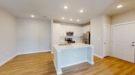 Located at 1001 Cox Grade Rd in Panama City Beach, Florida, this thoughtfully designed single-floor residence offers a clean, modern aesthetic throughout. The open-concept layout seamlessly connects the kitchen and living area, creating a bright and functional living space. The kitchen is a standout feature, showcasing white shaker-style cabinetry, light quartz countertops, a large center island with an integrated sink, and a full suite of stainless steel appliances including a refrigerator, range, and microwave. Recessed lighting illuminates the space, complementing the warm-toned luxury vinyl plank flooring that flows throughout the main living areas. The living room is airy and welcoming, equipped with a ceiling fan and French doors that open to an outdoor view, allowing natural light to pour in. The bedroom offers plush carpeting, a ceiling fan, and a bright window with exterior views, creating a comfortable retreat. The bathroom is finished with a white vanity featuring quartz countertops, a tiled tub-shower combination, and coordinating brushed nickel fixtures. A dedicated in-unit laundry area with a full-size washer and dryer adds everyday convenience. The overall ambiance is fresh, light, and move-in ready.