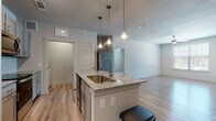 This single-floor, two-bedroom, two-bathroom residence offers a thoughtfully designed layout with contemporary finishes throughout. The kitchen serves as the heart of the home, centered around a granite-topped island with an undermount sink and seating space, illuminated by a trio of glass pendant lights. Gray shaker-style cabinetry, a white tile backsplash, and a full suite of stainless steel appliances—including a French door refrigerator, electric range, and built-in microwave—complete the well-equipped cooking space. Wood-look flooring extends through the kitchen and main living areas, lending warmth and continuity.

The living area is bright and open, featuring large windows that invite natural light and provide outdoor views, complemented by a ceiling fan. Built-in shelving adds functional storage near the hallway. Both bedrooms are carpeted and generously sized, with ceiling fans and ample natural light. The primary bedroom includes access to a private en-suite bathroom with a soaking tub, tiled surround, granite vanity, and wood-look flooring. The second bathroom offers a similar tub-shower combination and matching finishes, maintaining a consistent, modern aesthetic throughout the residence.