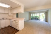 Located at 7955 Magnolia Ave in Riverside, California, this single-floor residence offers a clean, functional layout with a neutral color palette throughout. The living area is carpeted and filled with natural light from large windows and a sliding glass door that opens to lush outdoor greenery, creating a bright and inviting atmosphere. A front entry window further enhances the natural light in the main living space.

The kitchen is efficiently designed with white cabinetry, white appliances including a gas range and built-in microwave, a single-basin sink, and a peninsula counter that connects to the living area, providing a practical transition between spaces. The kitchen features dark hardwood-style flooring, contrasting with the soft carpet found throughout the rest of the unit.

The bedroom is generously sized with plush carpeting and a window offering pleasant views of surrounding trees. It includes access to a walk-in closet, providing ample storage. A secondary room or flex space is also accessible from the bedroom corridor.

The bathroom is finished in white with a large vanity featuring under-sink cabinetry, a wide mirror with overhead lighting, and a separate toilet area. The textured ceilings are consistent throughout the space, and central air vents indicate a climate-controlled environment, ensuring year-round comfort.