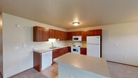 This single-floor residence offers a practical and comfortable layout designed for everyday living. The kitchen is a standout feature, showcasing rich medium-toned wood cabinetry that extends to the upper walls, providing generous storage throughout. Light-colored countertops complement the cabinetry, and the space is equipped with a full suite of white appliances including a refrigerator, electric range, built-in microwave, and dishwasher. Ceramic tile flooring runs throughout the kitchen, and a peninsula provides additional counter space and a natural transition to the living areas. The living room is generously sized, finished with soft wall-to-wall carpeting and warm neutral-toned walls. Natural light enters through a large window and a sliding glass door that opens to the outdoors, while a baseboard heating system and a wall-mounted air conditioning unit ensure year-round comfort. A chandelier adds a touch of character to the dining area. The bedrooms are carpeted and feature neutral walls and baseboard heating, with at least one room offering a walk-in closet with built-in shelving for organized storage. The bathroom is finished with tile flooring, a vanity with wood cabinetry, a large mirror, and a shower-tub combination, providing a clean and functional space.