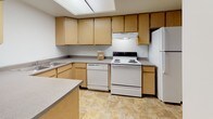 This two-story residence offers a practical and straightforward layout spread across two levels. The main floor centers around an open living area finished with warm hardwood-style flooring, which flows seamlessly toward the kitchen. A carpeted staircase with a white metal railing connects the two floors, accented by a ceiling-mounted light fixture overhead.

The kitchen is well-equipped with ample light wood cabinetry both above and below the countertops, offering generous storage throughout. Gray laminate counters wrap around the space in an L-shape, accompanied by a double stainless steel sink, an electric range, a dishwasher, and a refrigerator. Stone-patterned tile flooring and a skylight panel contribute to a bright, functional workspace.

The upper level houses the bedrooms, each featuring neutral carpet and white walls that create a clean, versatile canvas. One bedroom benefits from a window that brings in natural light. A dedicated walk-in closet with wire shelving provides organized storage. Two full bathrooms are present in the residence, each featuring a tub-shower combination, stone-tile flooring, a wood-framed vanity, and gray countertops, maintaining a consistent and cohesive aesthetic throughout.