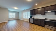 Located at 60 Beard Sawmill Rd in Shelton, Connecticut, this well-appointed single-floor unit offers a clean, modern design with consistent warm-toned hardwood-style flooring running throughout every room. The open-concept living and kitchen area forms the heart of the space, bathed in natural light from multiple large windows fitted with white horizontal blinds. The kitchen is fully equipped with dark espresso-finished cabinetry, granite countertops, a white subway tile backsplash, and a full suite of stainless steel appliances including a refrigerator, range, dishwasher, and microwave. Recessed lighting and flush-mount ceiling fixtures provide ample illumination throughout. The spacious living area flows seamlessly from the kitchen, offering generous room for furnishing and everyday living. A bedroom with a dedicated window provides a bright, private retreat. The bathroom features a full tub and shower combination with a curtain rod, complemented by a white vanity with granite countertops, a large mirror, and additional storage. Neutral gray walls, crisp white trim, and a thoughtful layout contribute to a cohesive, contemporary ambiance throughout this well-designed Shelton residence.