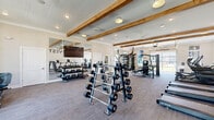 Located at 8251 Windsor Hill Blvd in North Charleston, SC, this single-floor fitness center is designed to support a comprehensive workout experience in a bright, welcoming environment. The space is characterized by its distinctive exposed wooden ceiling beams, recessed lighting, and neutral-toned carpet flooring, giving it a polished yet functional aesthetic.

The main workout area is generously proportioned, offering ample room for both cardio and strength training. Cardio equipment includes multiple treadmills, cycling bikes, elliptical machines, and a rowing machine, all positioned to take advantage of the natural light streaming through large windows and glass garage-style doors. These doors open to views of the outdoor pool and surrounding greenery, creating a seamless connection between the interior and exterior.

The strength training section is equally well-appointed, featuring a full rack of dumbbells, kettlebells, medicine balls, cable machines, and multi-functional weight equipment. Large wall mirrors visually expand the space and allow for proper form checks during exercise. Motivational phrases such as "Stronger Than" and "An Yesterday" are painted directly on the walls, adding an energizing and aspirational atmosphere. The overall design balances functionality with an inviting ambiance, making it a standout community amenity.