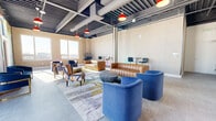 Located at 55 Washington St in East Orange, NJ, this single-floor lounge space offers a well-appointed, open-plan layout that blends industrial aesthetics with contemporary design. The exposed ceiling features dark-painted structural beams and visible ductwork, complemented by bold red pendant lights that add a striking visual contrast against the neutral tones of the space.

The main seating area is thoughtfully arranged with a mix of furniture styles, including a channeled tan leather sofa, plush cobalt blue barrel chairs, and eclectic striped accent chairs, all anchored by a large abstract area rug. Bar-height tables with modern stools provide additional seating options, while a woven hanging egg chair adds a unique design touch.

A standout feature is the full-height, floor-to-ceiling mural on one wall, bursting with vibrant swirls of color — creating a dramatic focal point. Adjacent to the mural, two sets of glass doors open to an outdoor area, flooding the interior with generous natural light and offering views of the surrounding cityscape.

A compact kitchenette area includes wood-grain cabinetry, a sink, and upper storage, adding functional utility to the space. Large windows throughout ensure the room remains bright and airy, reinforcing the open, welcoming atmosphere ideal for communal gathering or lounge use.