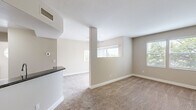 Located at 7149 Navajo Rd in San Diego, CA, this single-floor, one-bedroom, one-bathroom home offers a thoughtfully designed layout across a comfortable footprint. The kitchen is a standout feature, outfitted with rich warm-toned wood cabinetry, dark granite countertops, light hardwood-style flooring, and a full suite of stainless steel appliances including a gas range, built-in microwave, and dishwasher. Adjacent to the kitchen is a versatile built-in desk area with matching cabinetry and granite surfaces, ideal for a dedicated home office nook. The open living area is carpeted and bathed in natural light from multiple windows offering views of surrounding greenery, creating a warm and inviting atmosphere. The bedroom is a well-sized, carpeted retreat featuring a ceiling fan, a window with outdoor views, and direct access to a spacious closet with built-in shelving and hanging rods. The bathroom continues the granite and wood cabinetry theme, complemented by light hardwood-style flooring, a soaking tub, and a single vanity. A dedicated in-unit laundry room with a full-size GE washer and dryer, plus overhead storage cabinetry, adds everyday practicality. A connecting hallway ties all rooms together seamlessly.