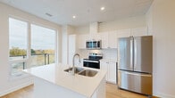 Located at 11 Wright Cres in Kingston, Ontario, this well-appointed 2-bedroom, 2-bathroom unit offers a clean, modern aesthetic throughout its thoughtfully designed single-floor layout. Light hardwood flooring flows seamlessly across all living areas, complementing the bright, neutral palette of white and warm beige tones.

The open-concept kitchen and living area serves as the heart of the unit, featuring white shaker-style cabinetry extending to the ceiling, white quartz countertops, a double-basin stainless steel sink set within a central island, and a full suite of stainless steel appliances including a refrigerator, electric range, and over-the-range microwave. A large window floods the kitchen with natural light and frames treetop views.

The spacious primary bedroom includes a large picture window and sliding glass doors opening to a private balcony with sweeping views of Kingston's skyline and surrounding greenery. The second bedroom is also generously sized with its own large window and city views. Both rooms feature light hardwood flooring and ample closet access via the hallway.

The two bathrooms are finished with neutral tile work, including a soaker tub with floor-to-ceiling subway-style tiling in one. A central hallway connects all rooms efficiently, completing this bright, modern urban residence.