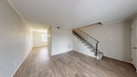 This two-story residence offers a well-organized layout across two levels, combining functional design with clean, updated finishes throughout. The main level features an open living and dining area anchored by durable wood-look flooring, textured ceilings, and crown molding. A large window at the front of the home allows natural light to fill the space, while a staircase with a black metal railing provides a visual focal point and connects to the upper floor. A sliding glass door in one of the main-level rooms opens to an outdoor patio area, bringing in additional natural light and outdoor views. The galley-style kitchen is well-appointed with white cabinetry, granite-style countertops, white appliances including an electric range and refrigerator, a double-basin sink, and wood-look flooring. A pantry or utility door offers additional storage. The bathroom features a full tub-shower combination, wood-look flooring, and a vanity with matching granite-style countertops. Upstairs, the carpeted bedrooms each include ceiling fans, closets with bifold doors, and a neutral color palette. The upper landing is accessible from the staircase, offering easy flow between rooms. Throughout, the home presents a clean, move-in-ready aesthetic with consistent finishes.