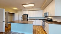 Located at 7800 Harkins Rd in Lanham, MD, this efficiently designed unit offers a thoughtful layout across a single floor. The kitchen serves as the heart of the space, showcasing white shaker-style cabinetry extending to the ceiling for generous storage, dark granite-style countertops, and a full suite of stainless steel appliances including a refrigerator, electric range, and over-the-range microwave. A central kitchen island with an undermount sink and matching countertop provides additional prep space and casual dining potential. Light wood-look flooring flows seamlessly from the kitchen into the open living area, which is filled with natural light from a wide bank of windows overlooking the surrounding neighborhood. The neutral warm-toned walls and clean white trim create a bright, cohesive ambiance throughout. A walk-in closet offers excellent storage capacity, outfitted with multi-tier wire shelving and hanging rods along two walls. The bathroom features large-format tile flooring, a soaking tub with tiled surround, and clean, minimalist fixtures. The overall design is modern and functional, making efficient use of every square foot.