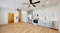 This thoughtfully designed single-floor unit maximizes its compact footprint through an open-concept layout that seamlessly integrates the kitchen and living area. Light-toned luxury vinyl plank flooring runs continuously throughout the main living spaces, contributing to a clean, cohesive aesthetic that enhances the sense of openness.

The kitchen is a standout feature, outfitted with white shaker-style cabinetry accented by matte black hardware, a farmhouse-style sink, and quartz countertops. A herringbone-patterned tile backsplash adds a refined visual detail, while stainless steel appliances — including a side-by-side refrigerator with ice and water dispenser, electric range, and over-the-range microwave — provide full functionality. A built-in wine rack above the refrigerator adds a distinctive touch.

The living area benefits from large, multi-pane windows fitted with horizontal blinds, allowing abundant natural light and views of the surrounding urban environment. Ceiling fans are installed throughout, ensuring comfortable airflow.

The bathroom features large-format beige tile flooring, a white vanity with ample storage, matte black fixtures, a wall-mounted cabinet, and a glass-enclosed shower. The overall design palette of bright whites and neutral tones gives the entire unit a modern, clean, and welcoming ambiance.